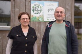 Une femme et un homme devant une pancarte "ici ferme bio"
