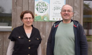 Une femme et un homme devant une pancarte "ici ferme bio"