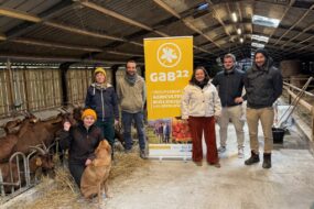 Trois femmes, trois hommes et un chien dans un bâtiment d'élevage de chèvres