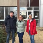 Un homme et deux femmes devant un bâtiment institutionnel