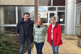 Un homme et deux femmes devant un bâtiment institutionnel