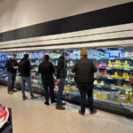 Des hommes habillés en sombre devant les rayons réfrigérés d'un supermarché