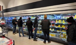 Des hommes habillés en sombre devant les rayons réfrigérés d'un supermarché