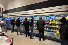 Des hommes habillés en sombre devant les rayons réfrigérés d'un supermarché