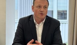 Un homme assis à une table en train de parler avec les mains croisées sur la table