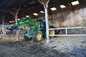 Un tracteur et une dérouleuse-pailleuse en fonctionnement dans une stabulation