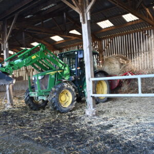 Un tracteur et une dérouleuse-pailleuse en fonctionnement dans une stabulation