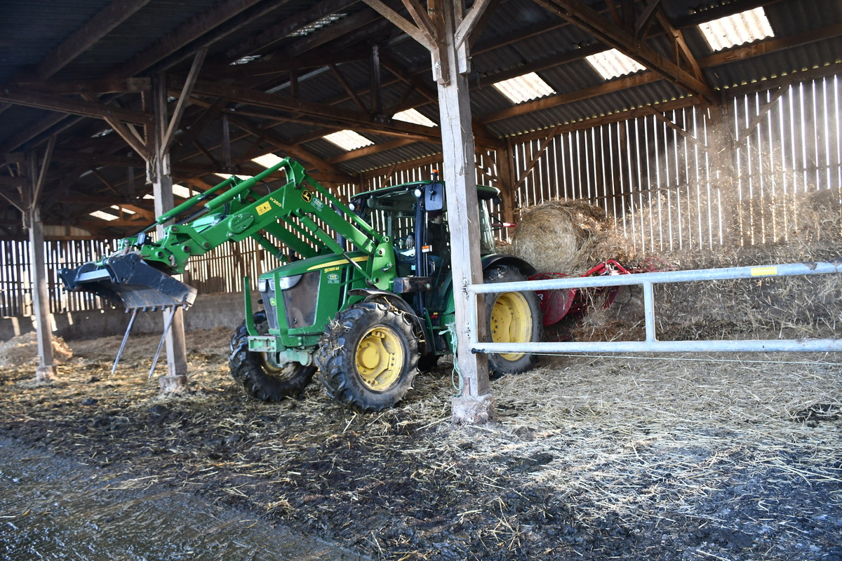 Un tracteur et une dérouleuse-pailleuse en fonctionnement dans une stabulation - Illustration Investissement ciblé dans une dérouleuse-pailleuse dès l’installation