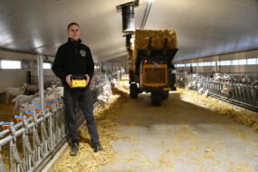 Un homme manie une dérouleuse-pailleuse à l'aide d'une télécommande dans un bâtiment d'élevage de chèvres