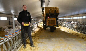 Un homme manie une dérouleuse-pailleuse à l'aide d'une télécommande dans un bâtiment d'élevage de chèvres