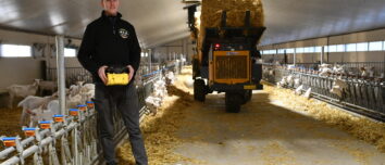 Un homme manie une dérouleuse-pailleuse à l'aide d'une télécommande dans un bâtiment d'élevage de chèvres