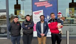 Quatre homme devant un magasin Ecomiam dont l'un porte un enfant en bas âge avec un bonnet.