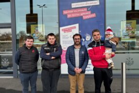 Quatre homme devant un magasin Ecomiam dont l'un porte un enfant en bas âge avec un bonnet.