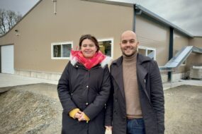 une femme et un homme devant un bâtiment de poules pondeuses