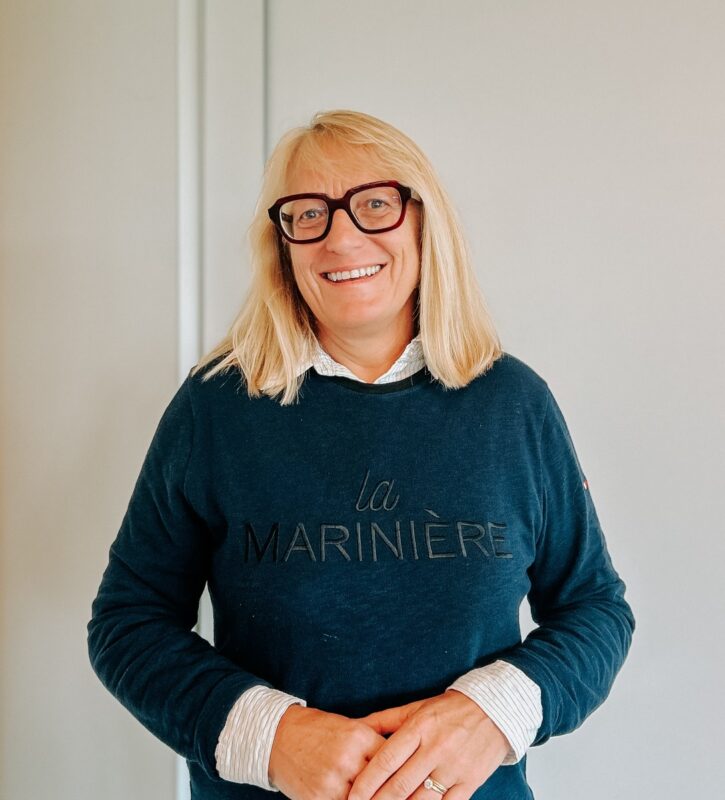 Une femme blonde aux cheveux longs, avec des lunettes noires, souriante