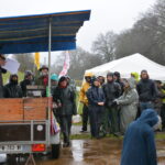Des manifestants écoutent, sous la pluie, une personne avec un micro installée sur une remorque couverte
