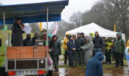 Des manifestants écoutent, sous la pluie, une personne avec un micro installée sur une remorque couverte