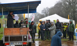 Des manifestants écoutent, sous la pluie, une personne avec un micro installée sur une remorque couverte