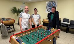 Trois hommes autour d'un baby-foot dans une salle avec plusieurs autres baby-foot
