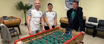 Trois hommes autour d'un baby-foot dans une salle avec plusieurs autres baby-foot