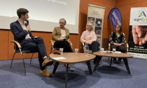 Des hommes et femmes assis derrière des tables basses dans une salle de réunion. Un homme parle dans un micro