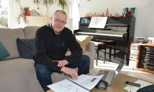 Un homme dans un camapé en train de travailler sur une table basse avec un piano derrière