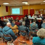 Une réunion rassemblant des gens face à des personnes assises derrière une table