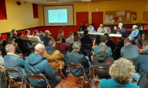 Une réunion rassemblant des gens face à des personnes assises derrière une table