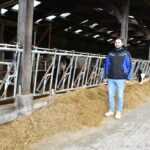 un homme devant des cornadis et une stabulation avec un robot de traite