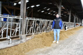 un homme devant des cornadis et une stabulation avec un robot de traite