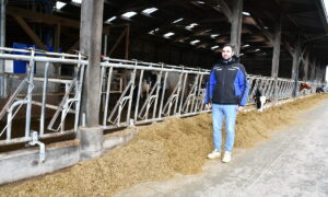 un homme devant des cornadis et une stabulation avec un robot de traite