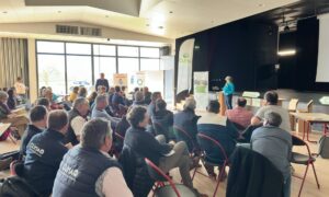 Un groupe de personne dans une salle dont une qui parle à la tribune