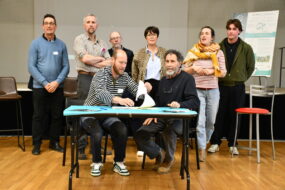 deux hommes assis signent un contrat avec des gens debout derrière