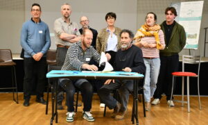 deux hommes assis signent un contrat avec des gens debout derrière