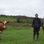 Un couple d'éleveur dans un champ aux côtés de l'une des vaches Pie Rouge de leur exploitation laitière.
