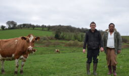 Un couple d'éleveur dans un champ aux côtés de l'une des vaches Pie Rouge de leur exploitation laitière.