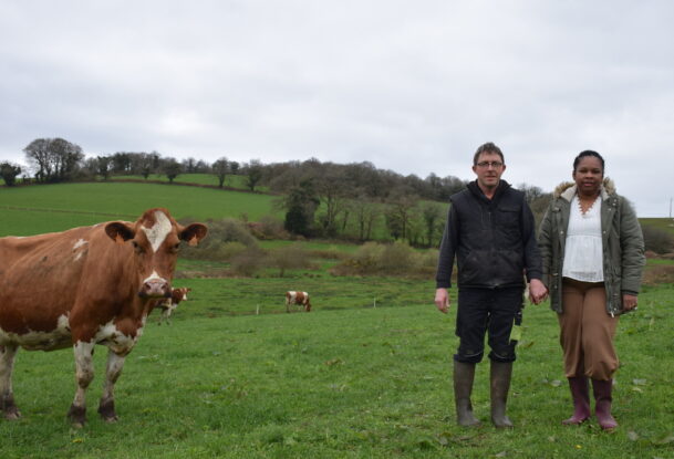 Un couple d'éleveur dans un champ aux côtés de l'une des vaches Pie Rouge de leur exploitation laitière.