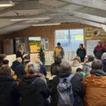 Une assemblée de personnes assises de dos face à cinq interlocuteurs debout