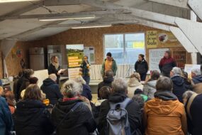 Une assemblée de personnes assises de dos face à cinq interlocuteurs debout