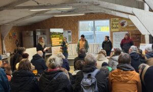 Une assemblée de personnes assises de dos face à cinq interlocuteurs debout