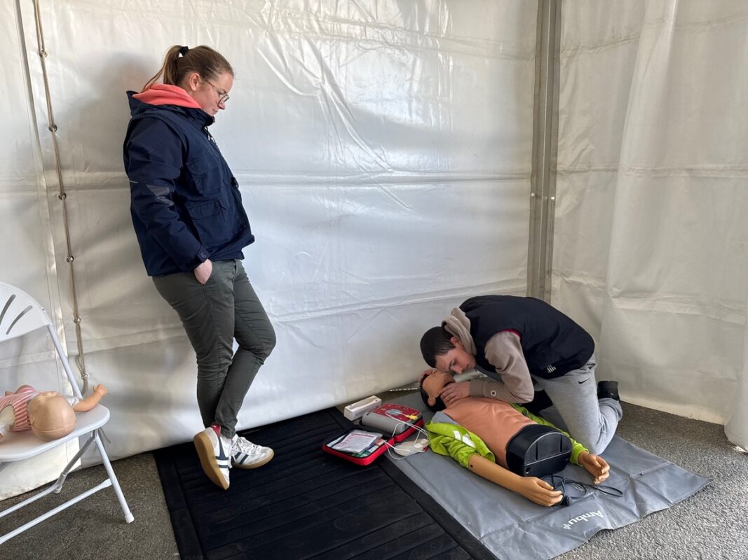 Un élève simule les geste s de premier secours sur un mannequin devant une femme