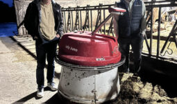 Deux hommes autour d'un robot repousse fourrage dans une stabulation bovine