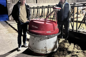 Deux hommes autour d'un robot repousse fourrage dans une stabulation bovine