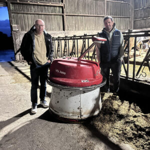 Deux hommes autour d'un robot repousse fourrage dans une stabulation bovine