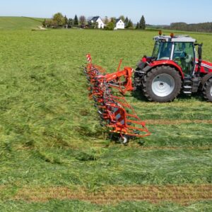 Un tracteur avec une faneuse attelée au champ