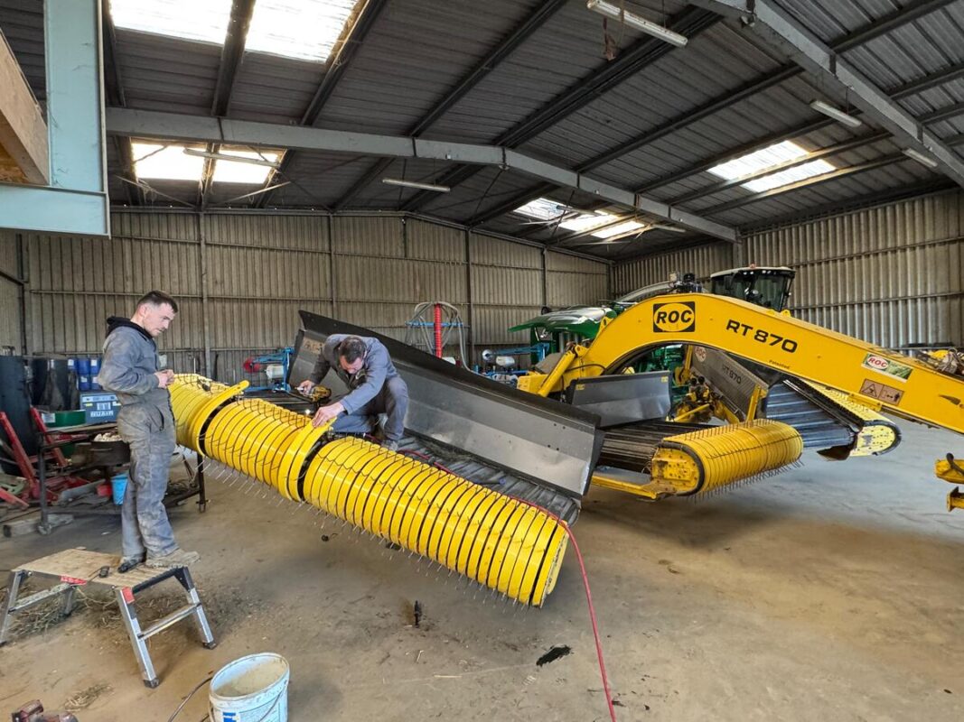 Deux hommes sont en train de réparer un andaineur à tapis dans le bâtiment d'une entreprise de travaux agricoles