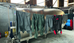 Des combinaisons de travail agricole en train de sécher sur un fil devant un tank à lait