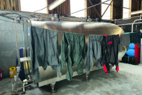 Des combinaisons de travail agricole en train de sécher sur un fil devant un tank à lait