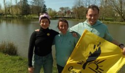 un homme et deux femmes au bord d'une rivière avec un drapeau de la Confédération Paysanne