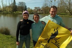 un homme et deux femmes au bord d'une rivière avec un drapeau de la Confédération Paysanne